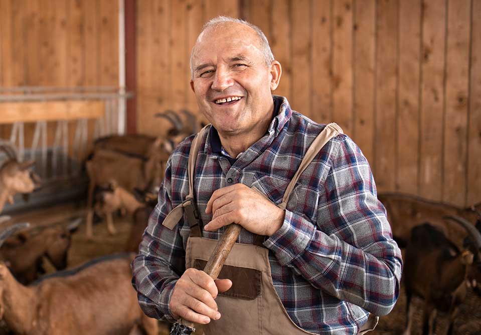 a farmer stands in a pen with animals smiling at the camera